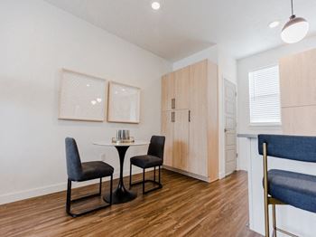 A dining area with a small table and two chairs and a kitchenette in the background